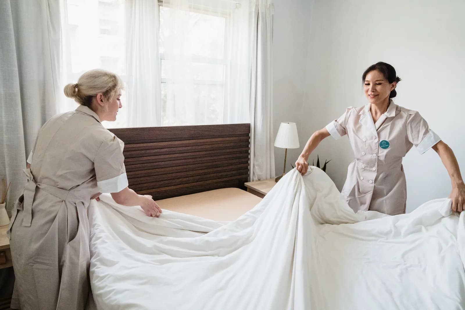 Two housekeepers putting fresh sheets on a bed